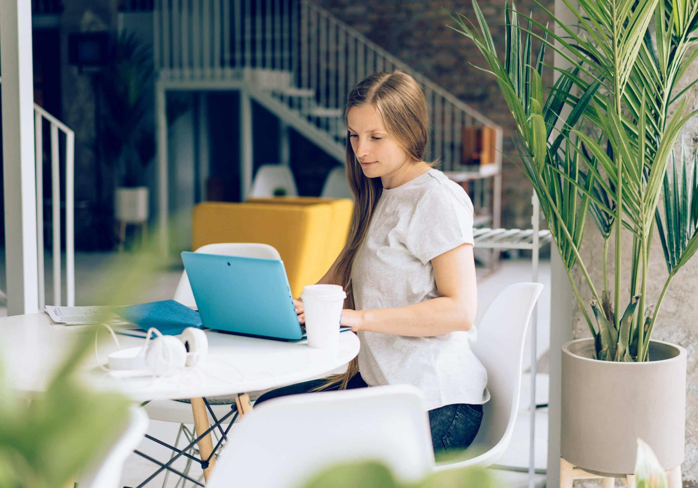 A woman working remotely on a computer at a desk by the window in a cafe. Communicate wirelessly on social media and chat.