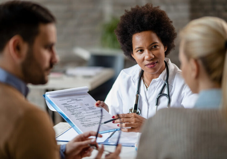 African American female doctor showing to a couple test results of their medical exam at clinic.